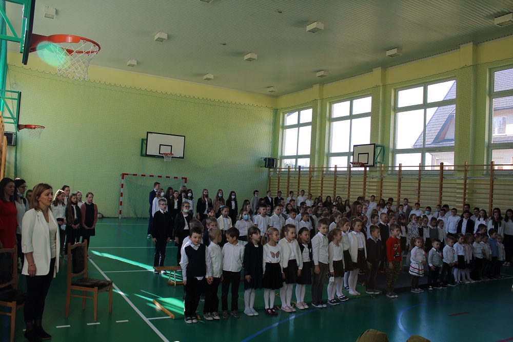 zdjęcie przedstawia wszystkich uczniów szkoły śpiewających Hymn Polski na sali gimnastycznej