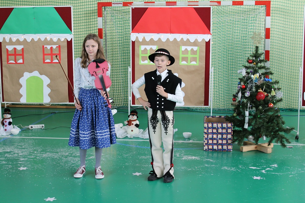 Zdjęcie przedstawia chłopca i dziewczynkę w strojach regionalnych składających życzenia z okazji Świąt Bożego Narodzenia