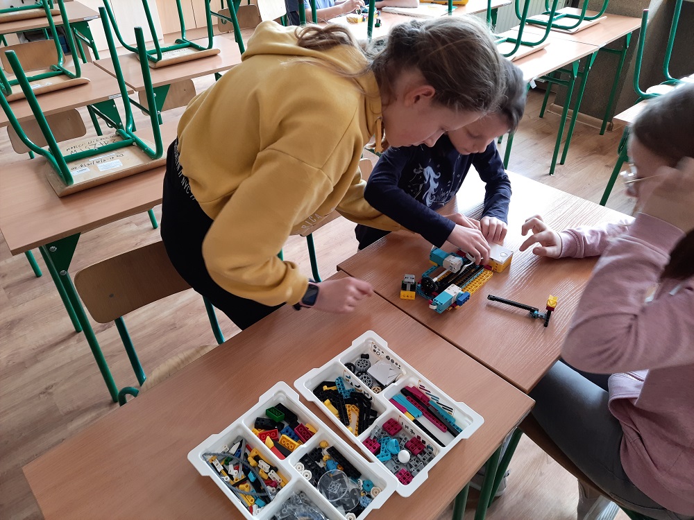 troje uczniów podczas budowania i testowania maszyny CNC z klocków Lego