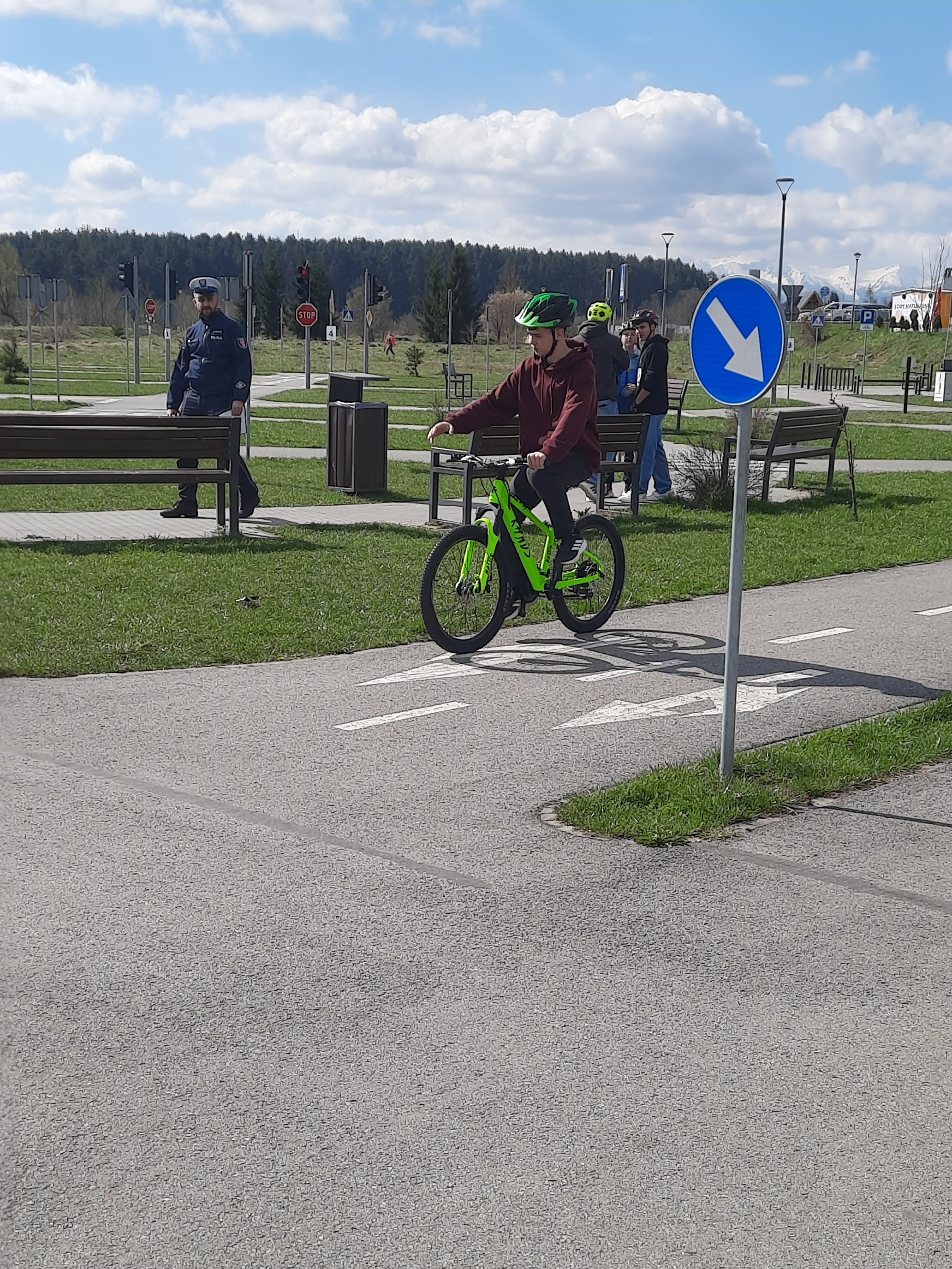 uczeń jadący na rowerze, w tle policjant