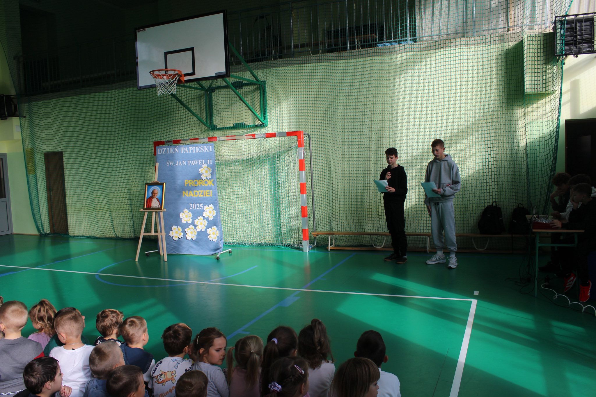 uczniowie na sali gimnastycznej podczas apelu z okazji "dnia papieskiego"
